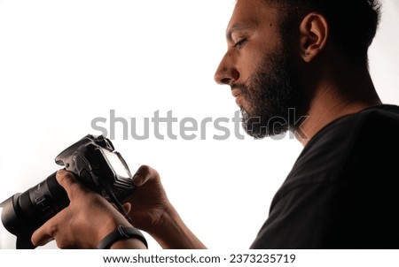 Photographer taking photos against white background in studio.
He uses a DSLR camera and looks at the photos he took. close-up shoulder scale