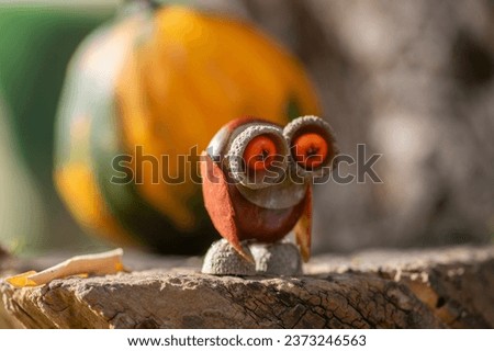 Funny chestnut owl bird animal with cute face berry eyes leaves wings on wooden bench, ripened pumpkins on background, traditional autumnal handcraft with children