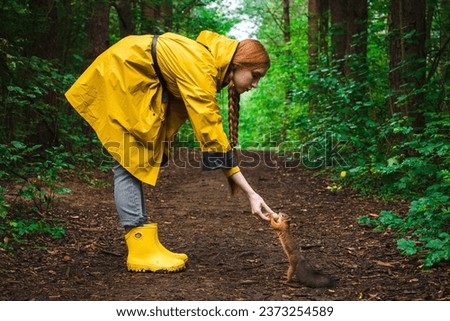 Woman in a yellow raincoat feeds a squirrel a walnut in the park.