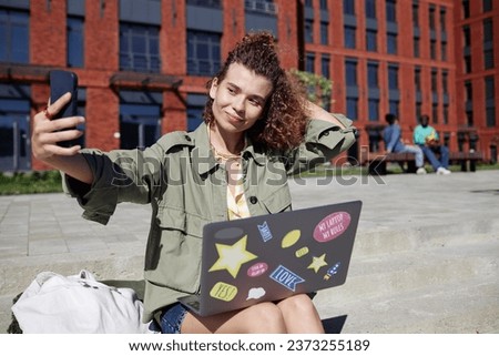 Portrait of young woman as student taking selfie photo outdoors on modern college campus, copy space
