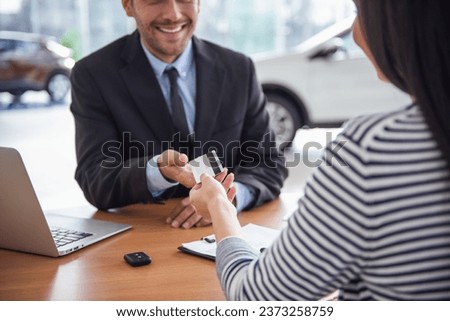 Visiting car dealership. Handsome sales manager is taking a credit card from the client and smiling