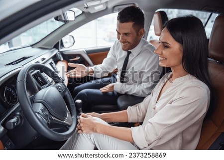 Beautiful young woman is talking to handsome car dealership worker while choosing a car in dealership