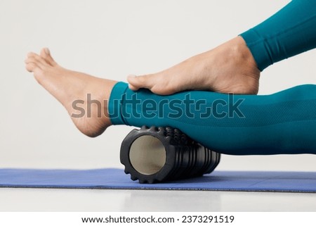 girl massages her legs on a roller and does yoga on a white background, massage roller for fitness and yoga, Home training