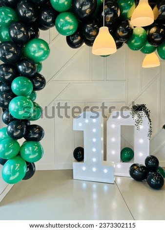 Indoor decoration with illuminanted 10 sign and green and black balloon with hanging light fixture to celebrate 10th business anniversary. 