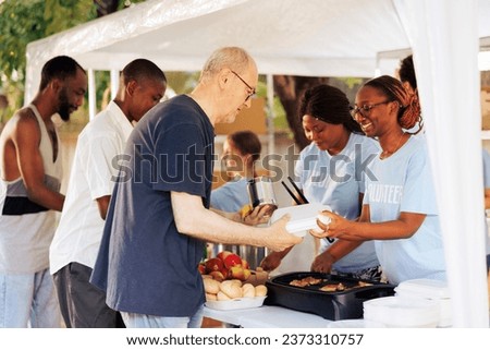 Homeless people from different backgrounds receive comforting meals from compassionate volunteers at local food bank. Community charity group supporting and sharing free food to the poor and needy. Royalty-Free Stock Photo #2373310757