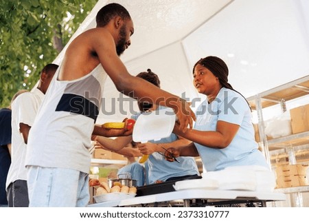 Young black woman helping the needy through food donation and volunteering in a community outreach program. Charity workers at food drive share fresh produce and necessities to poor, homeless people. Royalty-Free Stock Photo #2373310777