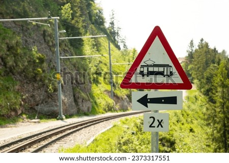 A closeup of a road sign directing people and cars to the left for a nearby train station in Switzerland on a sunny summer day with tracks in the background.