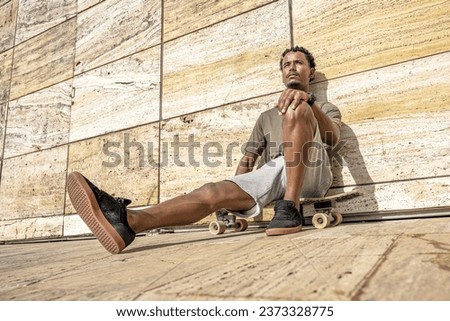 Surf skater resting sitting on his skateboard in an urban scene. Royalty-Free Stock Photo #2373328775