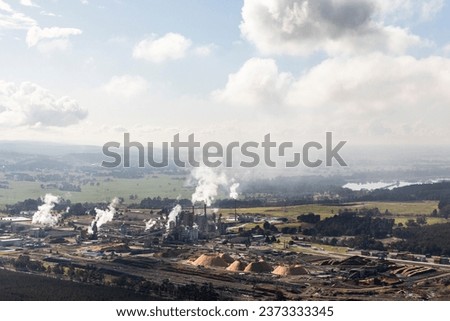 View of an industrial setting featuring a factory exterior, billowing smoke from thermal power plant stacks, and an active open-pit mine. Royalty-Free Stock Photo #2373333345