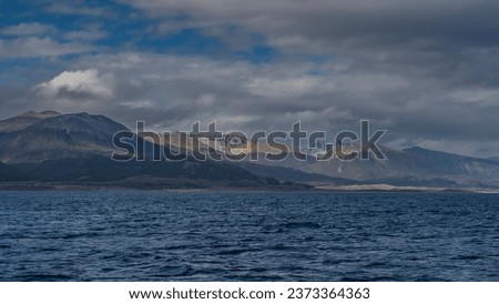 Beautiful Andean Martial mountain range against the background of blue sky and clouds. View from the Beagle Canal. Ripples on the water. Argentina. Tierra del Fuego Archipelago.