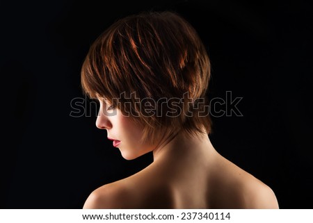 Side portrait of a young woman with short brown hair and brown glowing eyes. on a black background Royalty-Free Stock Photo #237340114