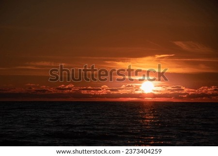 A perfect beach sunrise, with the sun creating a stunning orange hue on the horizon as the waves gently lap the shore