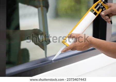 Male glass worker's hand uses silicone glue and glue to connect glass to aluminum. Royalty-Free Stock Photo #2373407443