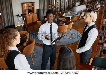 High angle portrait of restaurant manager talking to servers wearing classic uniforms during staff meeting in modern dining room Royalty-Free Stock Photo #2373418267