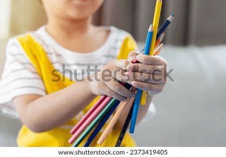 Close up of a child hand holding many colorful pencils while playing art paint at home. Back to school. Education, school, learning concept. Selective focus o hands.