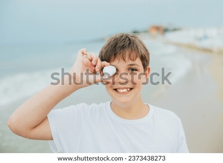 Portrait of a boy on the beach with a shell covering his eye against the backdrop of the sea