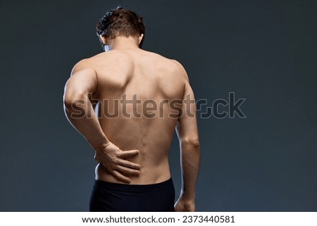 Rear view portrait of young brunette man posing, holding his muscular, healthy back isolated over dark grey studio background. Concept of men's health, beauty, fashion, wellness. Copy space. ad Royalty-Free Stock Photo #2373440581