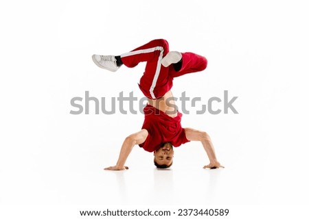 Headspin. Stylishly dressed man dancing breakdance, freestyle elements standing on head at dancehall against white studio background. Concept of youth culture, sport, lifestyle. Copy space Royalty-Free Stock Photo #2373440589