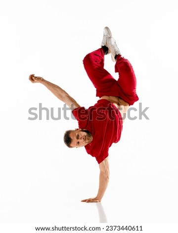 Young attractive man, guy, dancer wearing stylishly cloth dancing hip-hop, breakdance elements, freezes against white background. Concept of youth culture, sport, active lifestyle. Copy space.