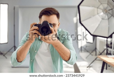 Young male photographer taking photos with dslr camera. Front view shot of handsome photographer shooting in studio with digital camera and professional lighting equipment