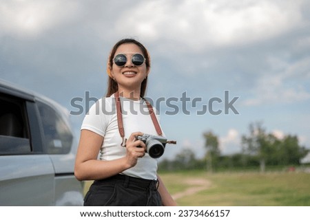 An attractive and positive young Asian woman in sunglasses travels by car, arriving at her destination in the countryside. road trip, holiday, vacation