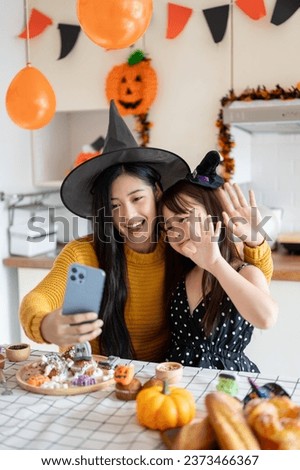 A cute and happy young Asian girl in a Halloween costume is having fun, taking selfies or taking video with her mom, and celebrating Halloween at home together.