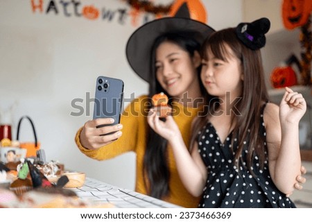 A cute and happy young Asian girl in a Halloween costume is taking selfies with her mom, celebrating Halloween at home together. selective focus image
