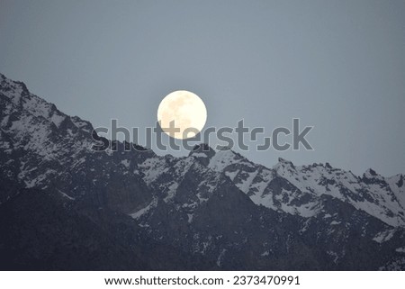 On a night with a full moon, the darkness is illuminated by a bright, silvery orb that hangs in the sky. The mountains, once shrouded in shadows, are now bathed in the moon's glow. Their jagged peaks  Royalty-Free Stock Photo #2373470991