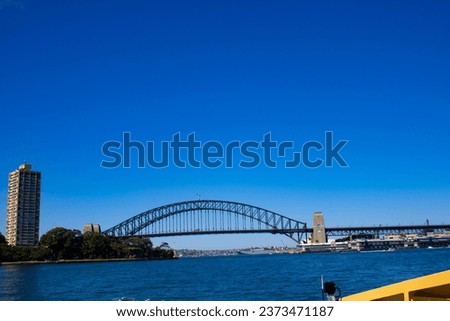 Capture the beauty of  Harbor Bridge in Sydney, New South Wales. This mesmerizing photo, taken from a boat, showcases the bridge in all its splendor, framed by lush greenery .