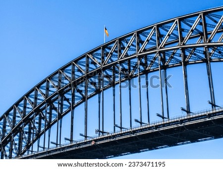 Captured up close, this stunning photograph of the iconic Sydney Harbour Bridge in New South Wales, Sydney City, showcases its grandeur. The focal point is a gracefully waving flag .