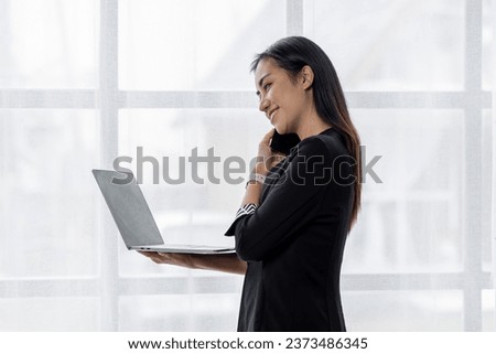 Portrait of young asian woman, company worker in documents smiling and holding digital Laptop, standing over office background