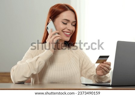 Happy woman with credit card using smartphone for online shopping at wooden table indoors