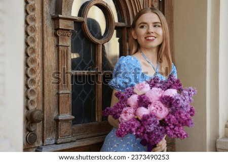 Beautiful woman with bouquet of spring flowers near building outdoors, space for text