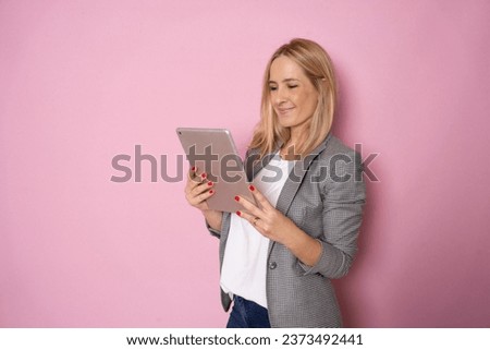 Portrait of happy young blonde business woman using tablet isolated against pink background. Smiling pretty girl holding a digital tablet computer. Modern technologies and business