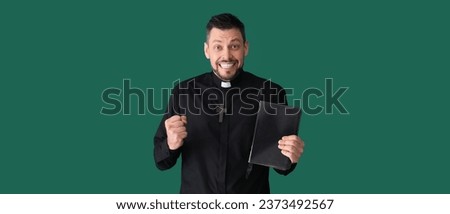 Happy priest with Bible on green background 