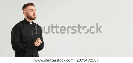 Young priest praying to God on light background with space for text