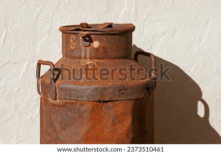 OLD RUSTED METAL MILK CAN AGAINST A WHITE WALL Royalty-Free Stock Photo #2373510461