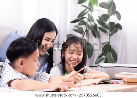 Cheerful Asian mother spend time with two sibling kids teaching homework drawing picture together in living room at home, free time children on holiday bonding happy relationship with mom parenthood