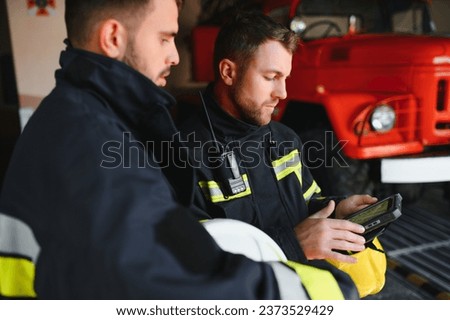 Portrait of two firefighters in fire fighting operation, fireman in protective clothing and helmet using tablet computer in action fighting.