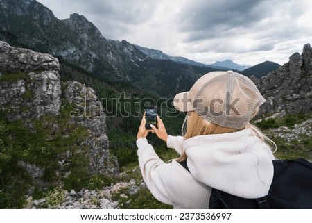 A girl takes a photo with her phone high in the Tatra mountains, the sky is overcast with storm clouds, photo from the back. High quality photo