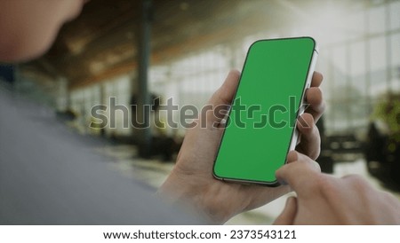 CU 30s Caucasian male holding a generic smart phone in vertical orientation, airport terminal in the background, green screen chroma key