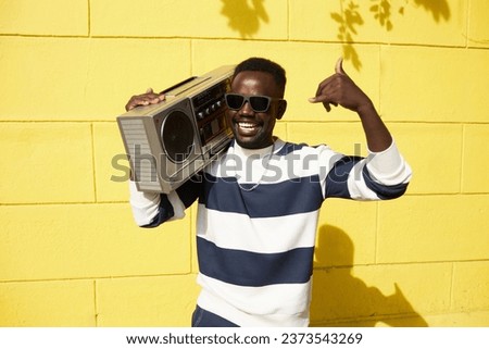 Vibrant waist up portrait of funky Black man holding boombox outdoors and dancing to music, copy space