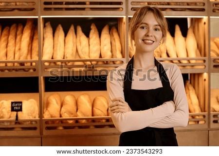 Waist up portrait of young woman standing behind counter in artisan bakery and smiling at camera with arms crossed, copy space Royalty-Free Stock Photo #2373543293