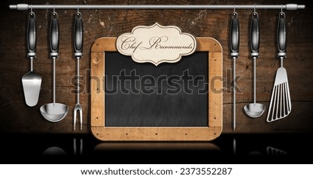 Empty blackboard with wooden frame with copy space and a label with text Chef Recommends, set of kitchen utensils made of stainless steel and black plastic on a wooden wall. 