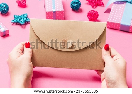 Top view of woman holding an envelope on pink background made of holiday decorations. Christmas time concept.
