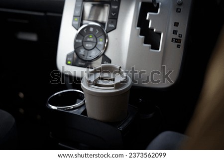 A travel coffee mug or tumbler in a car cup holder on the driver's seat.  Royalty-Free Stock Photo #2373562099