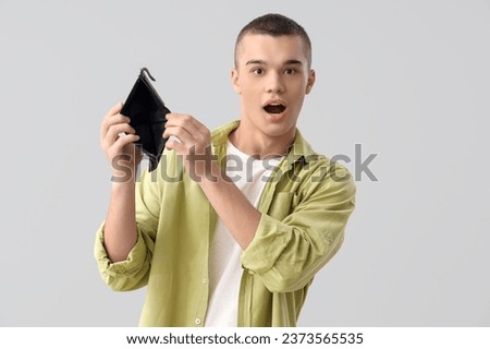 Shocked young man with empty wallet on light background