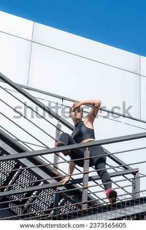 Brave athletic woman standing high on modern building outdoors in black sport running clothing, street style grunge fitness model