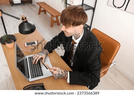 Young businessman with credit card using laptop at table in office