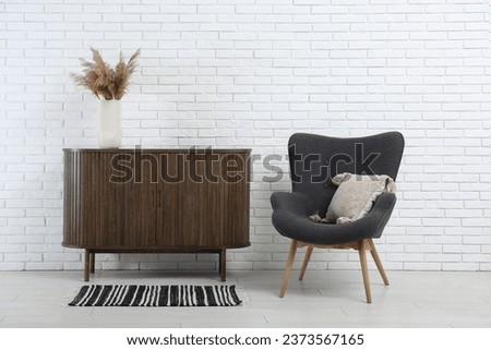 Stylish armchair and wooden cabinet near light brick wall